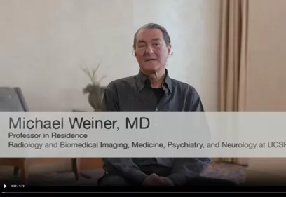 Video thumbnail featuring Michael Weiner, MD, seated indoors during an interview. On-screen text identifies him as a Professor in Residence in Radiology and Biomedical Imaging, Medicine, Psychiatry, and Neurology at UCSF. A large play button overlay indicates the image links to a video discussing Alzheimer's disease research and the Alzheimer's Disease Neuroimaging Initiative (ADNI).