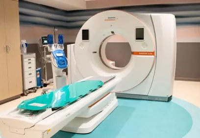 A CT scan room featuring a Siemens SOMATOM X.cite scanner with the patient table extended, surrounded by medical equipment and storage cabinets in a clean, modern clinical setting.