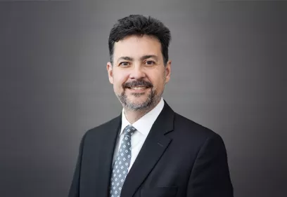 Christopher Hess, MD, PhD, wearing a dark suit and patterned tie, smiles at the camera in a professional portrait against a gray background.