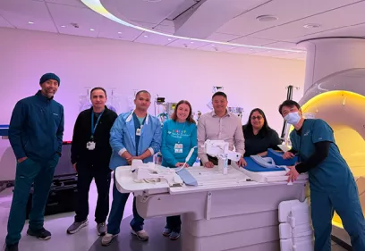 Group of seven healthcare professionals standing around an MRI scanner in a clinical imaging suite, posing together beside the patient table and scanner.
