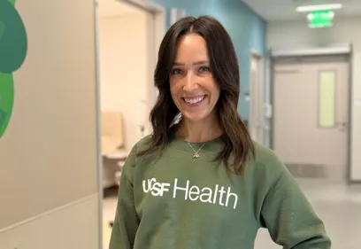 Woman wearing a green UCSF Health sweatshirt in a hospital hallway.