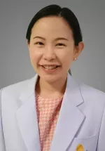 Professional headshot of Tunlada, a smiling woman with dark hair pulled back wearing a white coat and patterned blouse against a gray background.