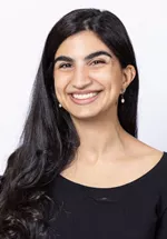 Portrait of Alina Hasanain, MD smiling, wearing a navy blazer over a light top against a light gray background.