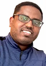 Head-and-shoulders portrait of a person smiling at the camera, wearing rectangular glasses and a navy quarter-zip pullover. The background is plain light gray, with the person's head slightly tilted toward the camera.