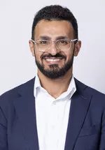 Portrait of Gais Tarat, MD with a neutral expression, wearing a light blue button-down shirt against a light gray background.