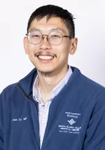 Portrait of James Zou, MD smiling, wearing a black top and small hoop earrings against a light gray background.