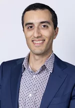 Portrait of Keon Mahmoudi, MD smiling, wearing glasses, a white shirt, and a navy blazer against a light gray background.