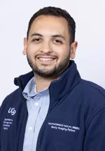 Portrait of Mohammad Nouh, MBBS smiling, wearing a light blue button-down shirt and a navy UCSF fleece jacket against a light gray background.