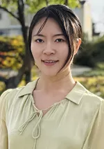 Headshot of Nan Wang wearing a light green blouse outdoors with trees and soft greenery in the background.