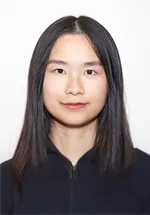 Head-and-shoulders portrait of a person with long, straight dark hair, looking directly at the camera with a neutral expression. They are wearing a black zip-up top against a plain light background.