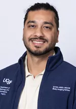 Portrait of Syed Abidi smiling, wearing a light blue button-down shirt and a navy UCSF fleece jacket against a light gray background.