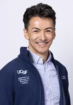 Portrait of Zachary Hoskins, MD smiling, wearing a navy blazer over a patterned button-down shirt against a light gray background.
