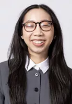 Smiling person wearing round glasses and a gray collared top against a light gray background.