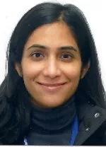 Headshot of a woman with long dark hair wearing a dark jacket, smiling softly against a light background.