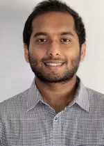Headshot of Rajath Ramegowda wearing a gray checkered button-down shirt against a light gray background.