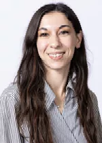 Smiling person with long dark hair, wearing a striped button-up shirt against a light gray background.
