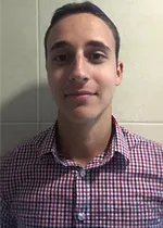 Head-and-shoulders photo of a person wearing a red, blue, and white checkered button-down shirt, facing the camera against a light tiled wall.