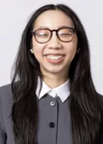 Smiling person wearing round glasses and a gray collared top against a light gray background.