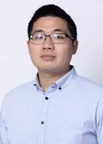 Person wearing glasses and a light blue button-up shirt against a light gray background.