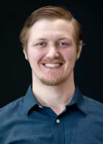 Professional headshot of Tyler Cork smiling, wearing a dark blue collared shirt against a black background.