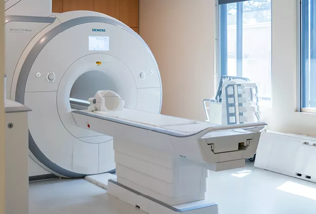Empty Siemens Magnetom Skyra 3 Tesla MRI scanner with patient table extended in a bright imaging suite near a window.