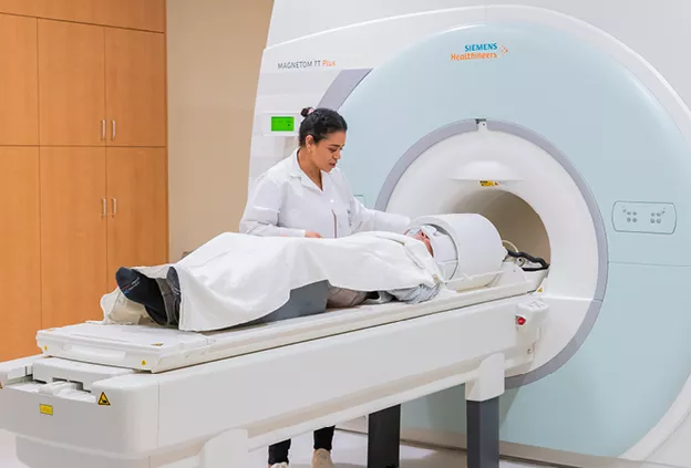 MRI technologist positioning a patient on the table of a Siemens Magnetom 7 Tesla MRI scanner inside a clinical imaging room.