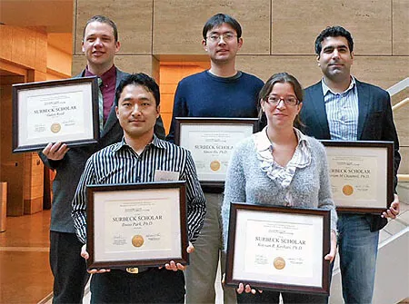 Group of five people standing indoors on a staircase, each holding a framed certificate. Three people stand in the back row and two in the front row, all smiling toward the camera.