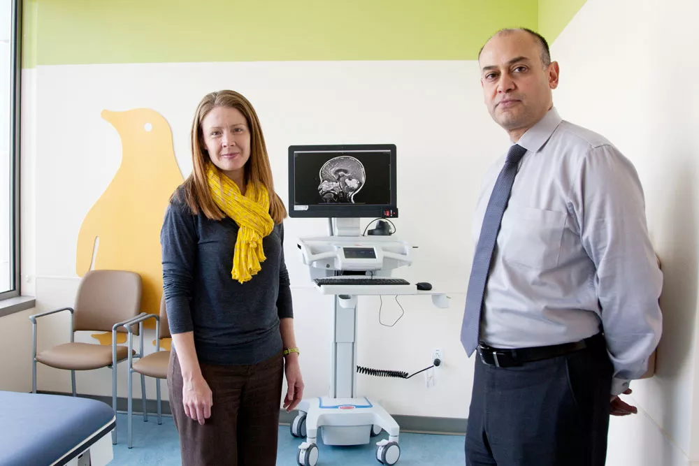 Heather Fullerton and Nalin Gupta stand in an examination room in front of a computer screen showing a pediatric brain scan.