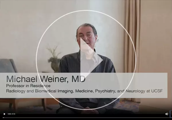 Video thumbnail featuring Michael Weiner, MD, seated indoors during an interview. On-screen text identifies him as a Professor in Residence in Radiology and Biomedical Imaging, Medicine, Psychiatry, and Neurology at UCSF. A large play button overlay indicates the image links to a video discussing Alzheimer's disease research and the Alzheimer's Disease Neuroimaging Initiative (ADNI).