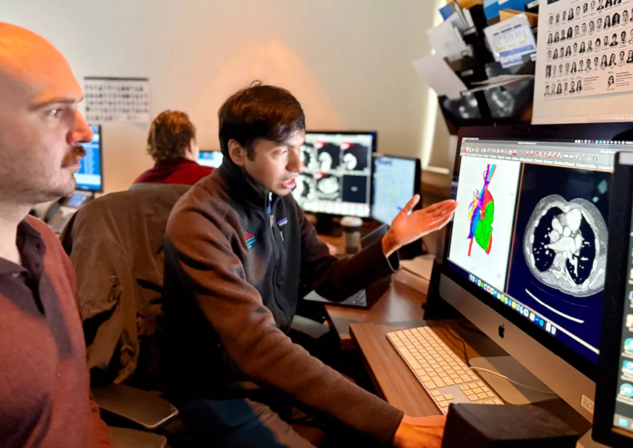 A radiologist and physician review advanced 3D cardiothoracic CT images on a workstation, collaborating on image analysis and treatment planning.