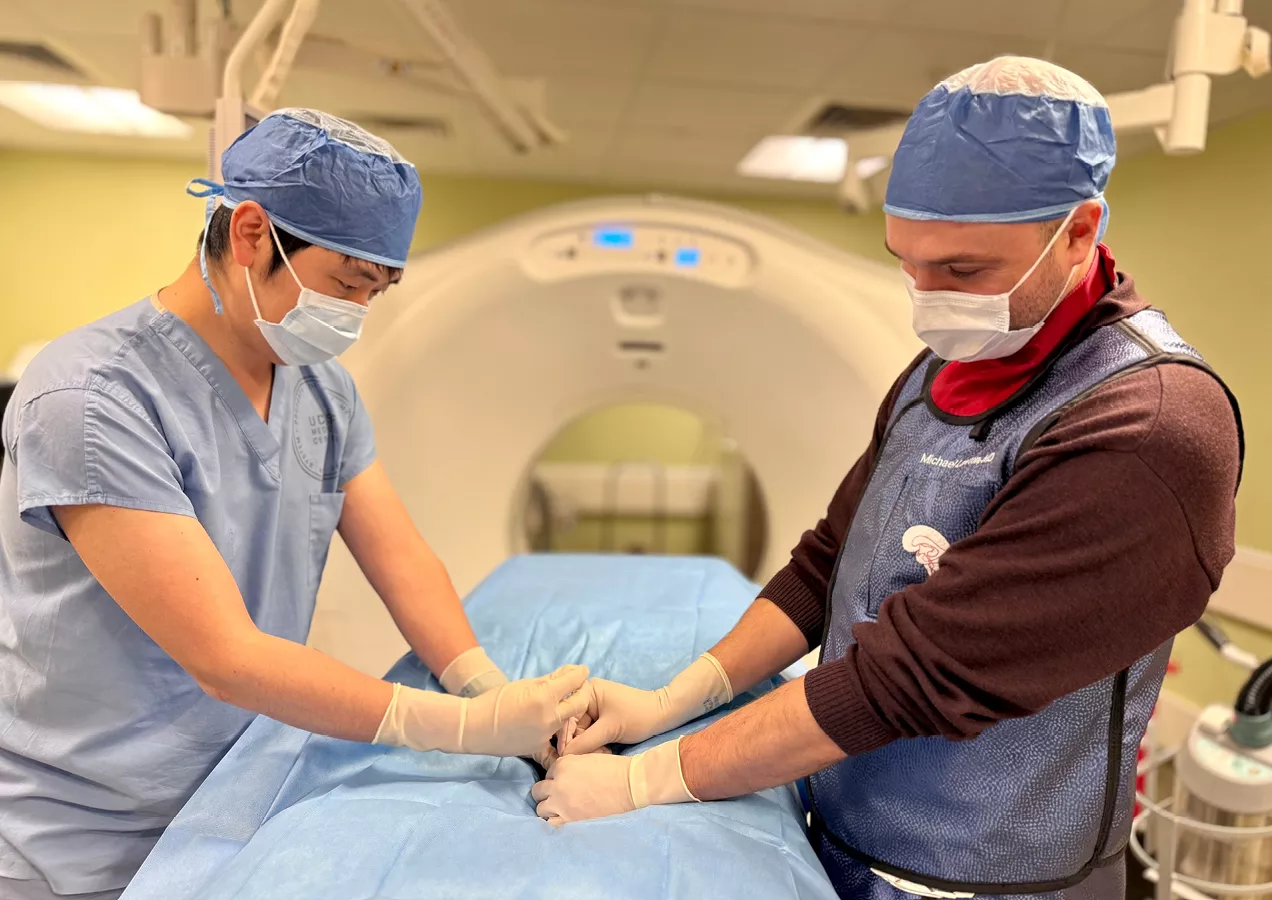 A physician and interventional radiologist perform a CT-guided minimally invasive procedure in a medical imaging suite, demonstrating precision image-guided patient care.