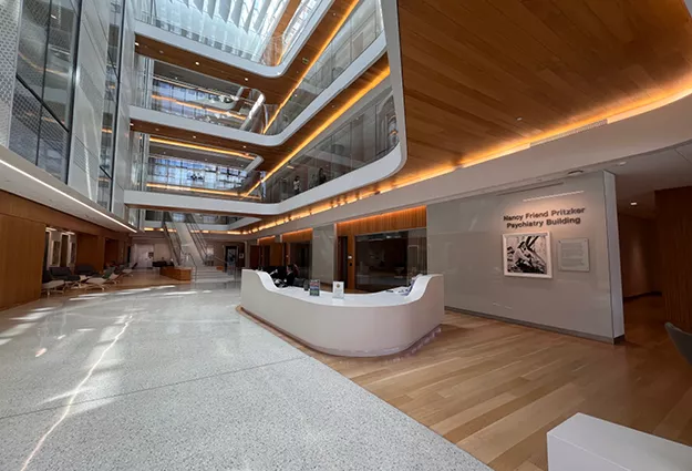 Bright, multi-story atrium of the Nancy Friend Pritzker Psychiatry Building with a central reception desk, wood finishes, and glass-lined upper floors.