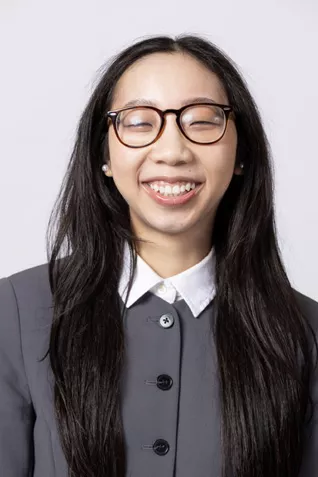 Smiling person wearing round glasses and a gray collared top against a light gray background.
