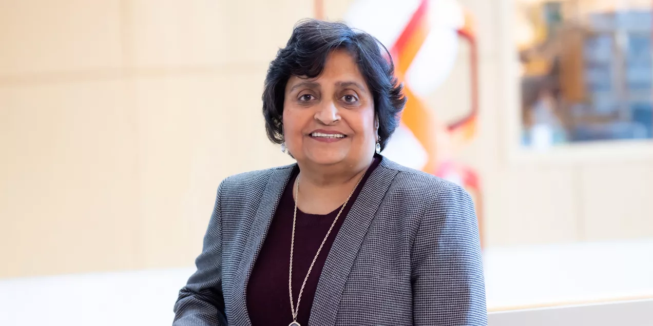 Portrait of a smiling woman wearing a gray blazer and burgundy top in a bright indoor setting.