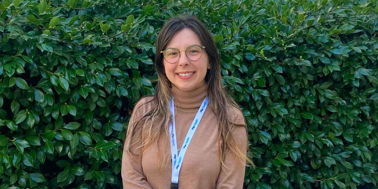 Portrait of a smiling woman wearing glasses and a UCSF Health lanyard in front of a leafy green hedge.