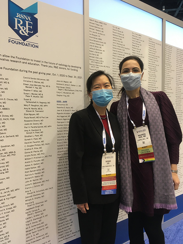 Two women wearing masks posted in front of a sign at a conference
