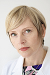 Professional headshot of a woman with short blonde hair wearing a white coat, looking slightly to the side.