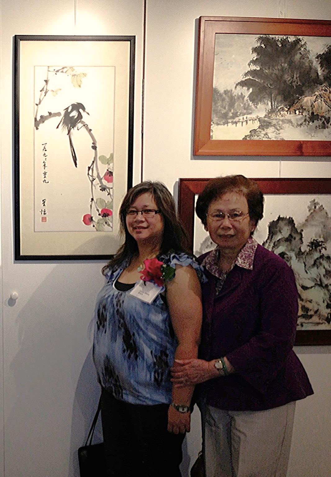 Two women standing in front of a traditional Chinese brush painting.