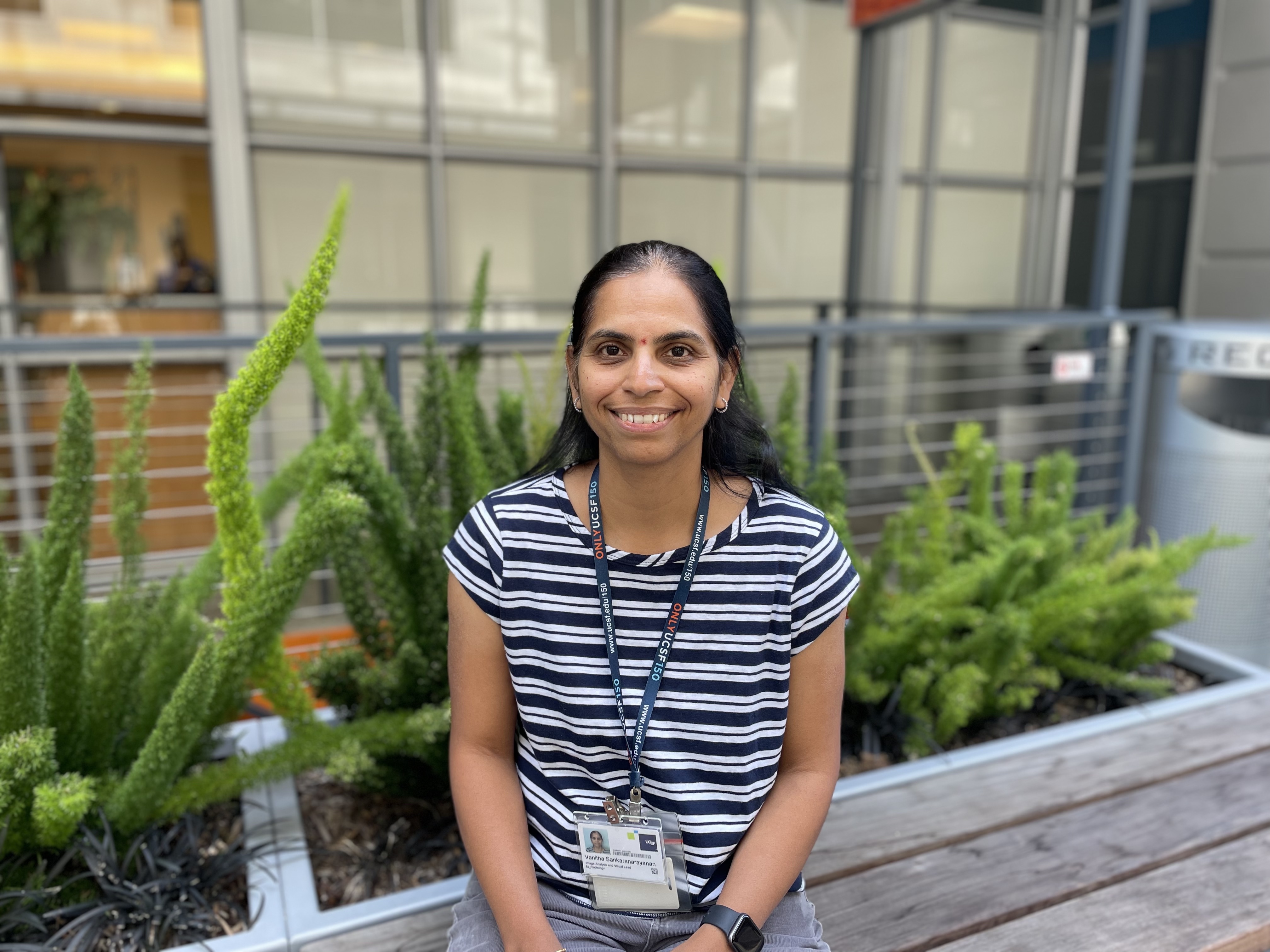 Woman smiling sitting on a bench in front of an office building.